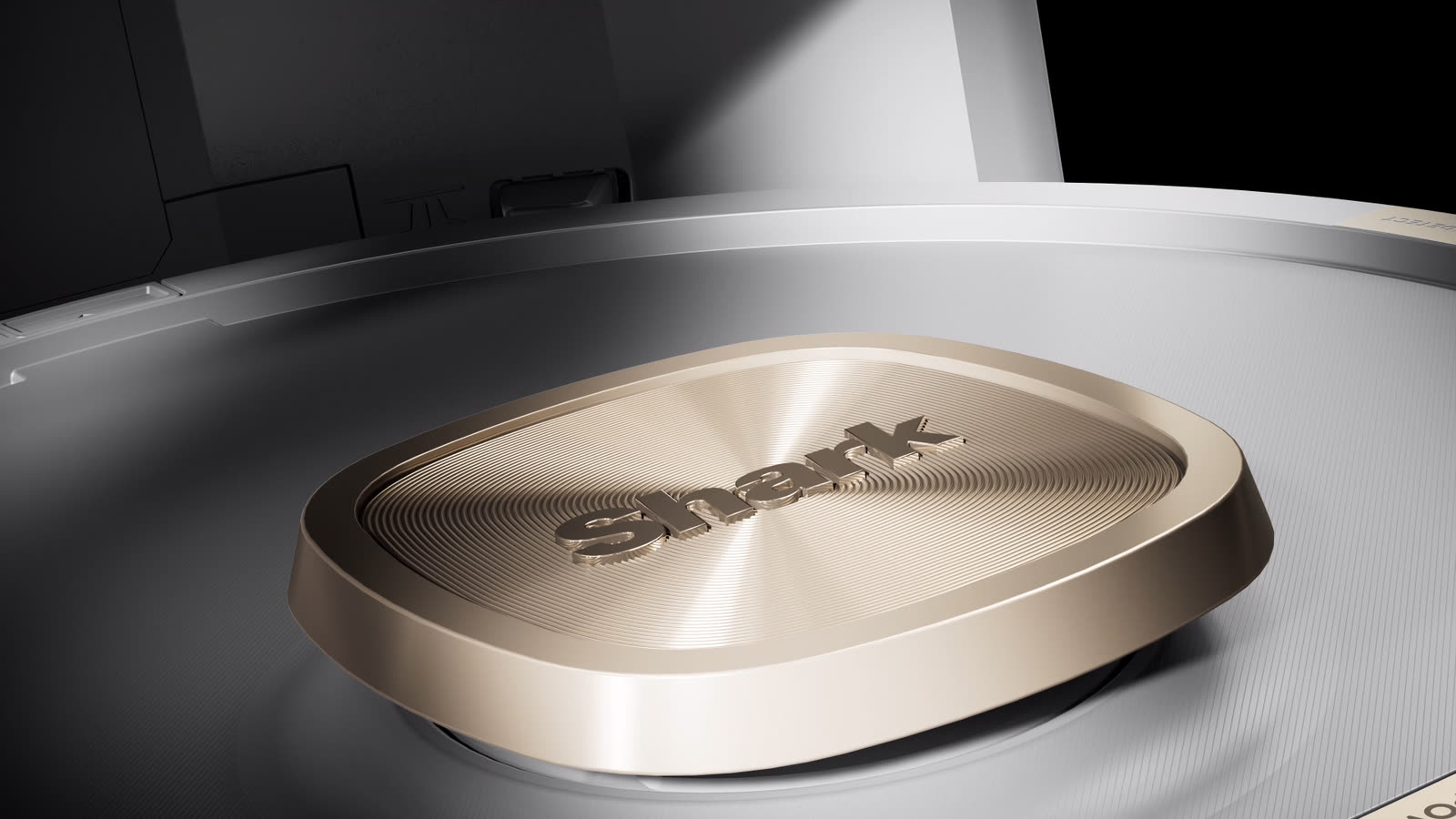The robot vac's champagne metallic top and gold Shark badge under dramatic light